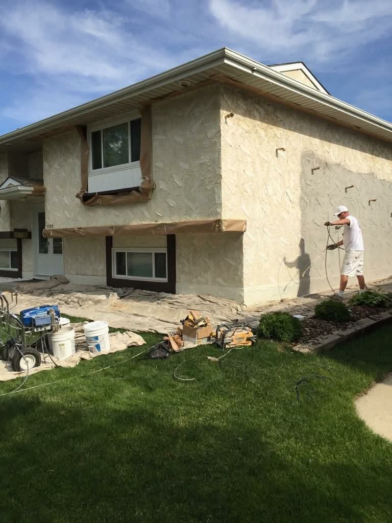 Faded cream stucco exterior being masked and sprayed